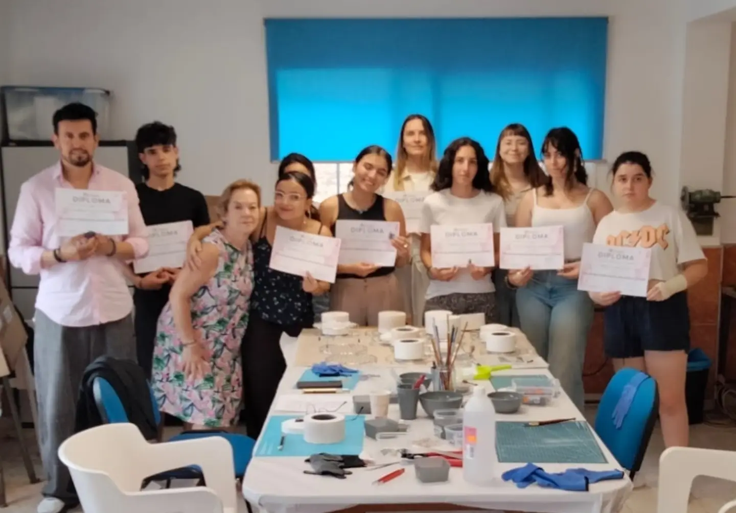 Alumnado con sus diplomas del curso de vitrofusión, junto a la mesa de trabajo con el material del taller