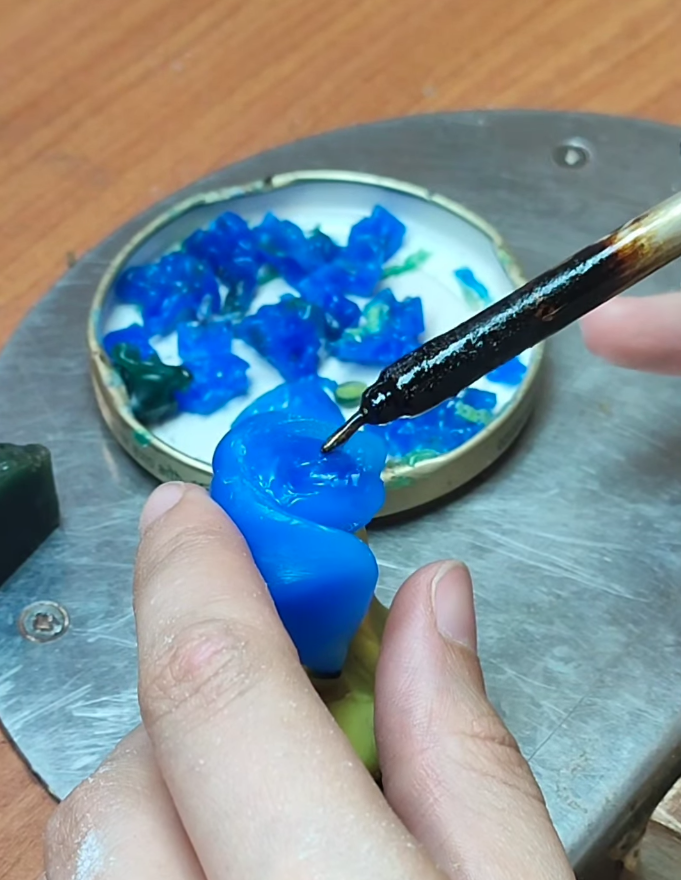 Modelado de una pieza de cera azul añadiendo cera fundida con un lápiz calentador